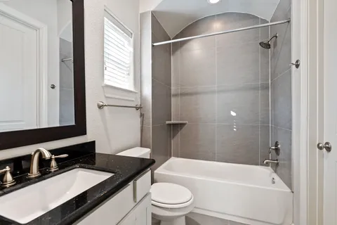 a bathroom with a granite countertop bathtub shower sink vanity and toilet