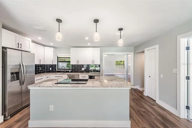 a kitchen with stainless steel appliances granite countertop a refrigerator a stove a sink dishwasher a oven with white cabinets and wooden floor