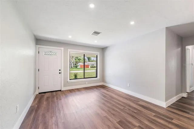 a view of an empty room with wooden floor and a window