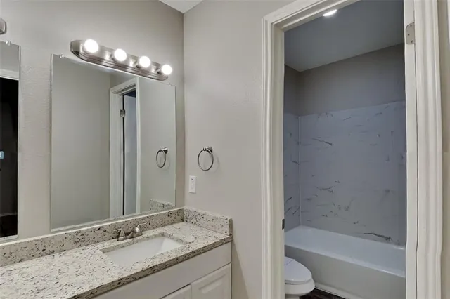 a bathroom with a granite countertop sink a toilet and shower