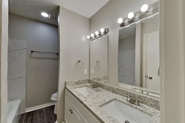 a bathroom with a granite countertop sink a toilet a shower and a mirror