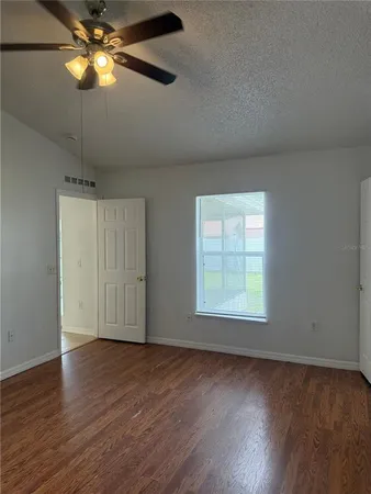 an empty room with wooden floor chandelier fan and windows