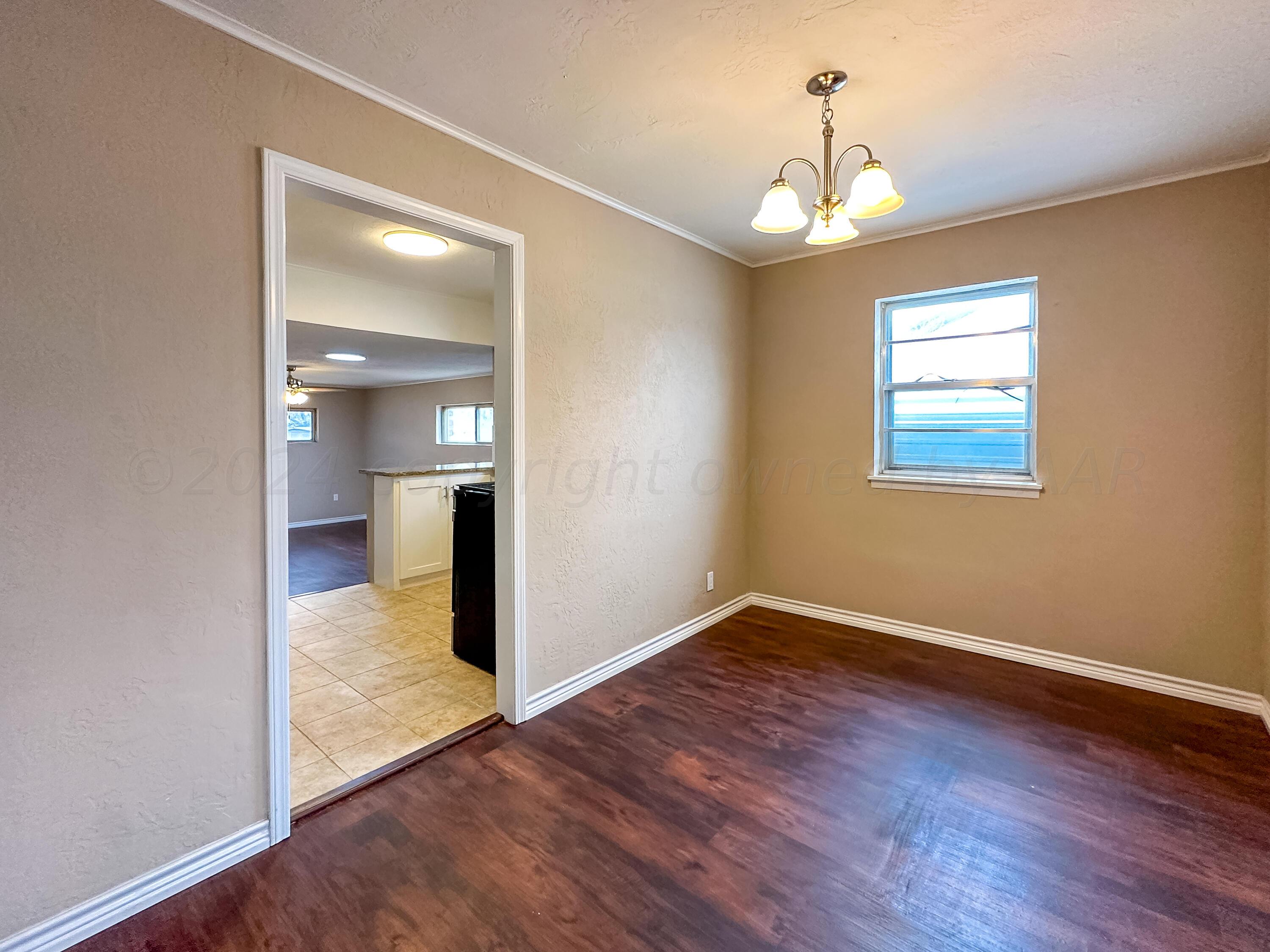 1103 Madison Street Borger, TX 79007 - Photo 7 of 16 an empty room with wooden floor chandelier and windows
