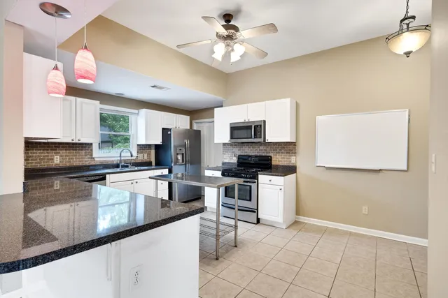 a kitchen with stainless steel appliances granite countertop a sink a stove a microwave oven a refrigerator with white cabinets and wooden floor