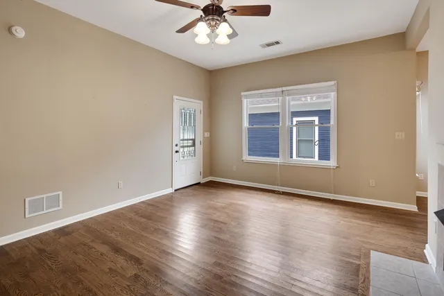 an empty room with wooden floor chandelier fan and windows