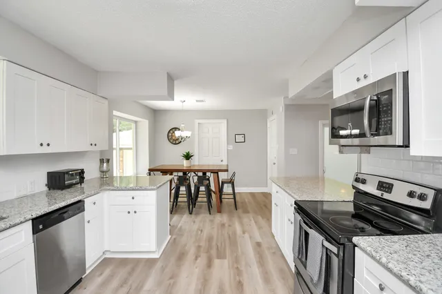 a kitchen with granite countertop a stove top oven a sink dishwasher a dining table and chairs with wooden floor