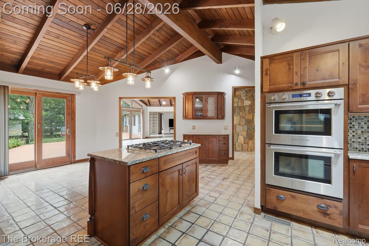 8475 Knox Road Clarkston, MI 48348 - Photo 23 of 71 Kitchen featuring vaulted wood-paneled ceilings with exposed beams, an island with a gas cooktop, double wall ovens, wood cabinetry, and square tile flooring