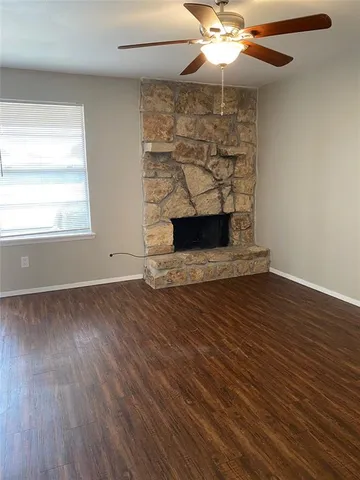an empty room with wooden floor a chandelier fan and a fireplace