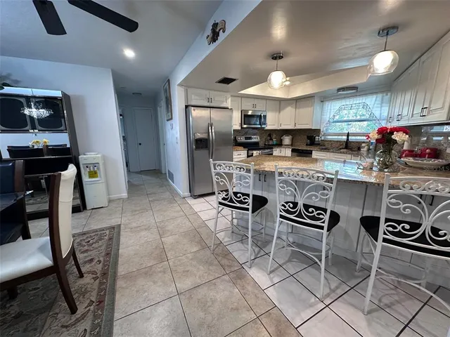 a kitchen with stainless steel appliances kitchen island granite countertop a stove a refrigerator a sink a dining table and chairs with white cabinets
