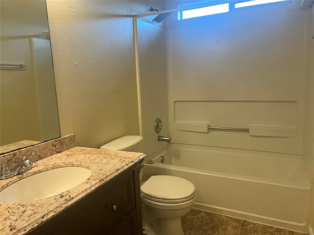 a bathroom with a granite countertop bathtub sink vanity mirror and toilet