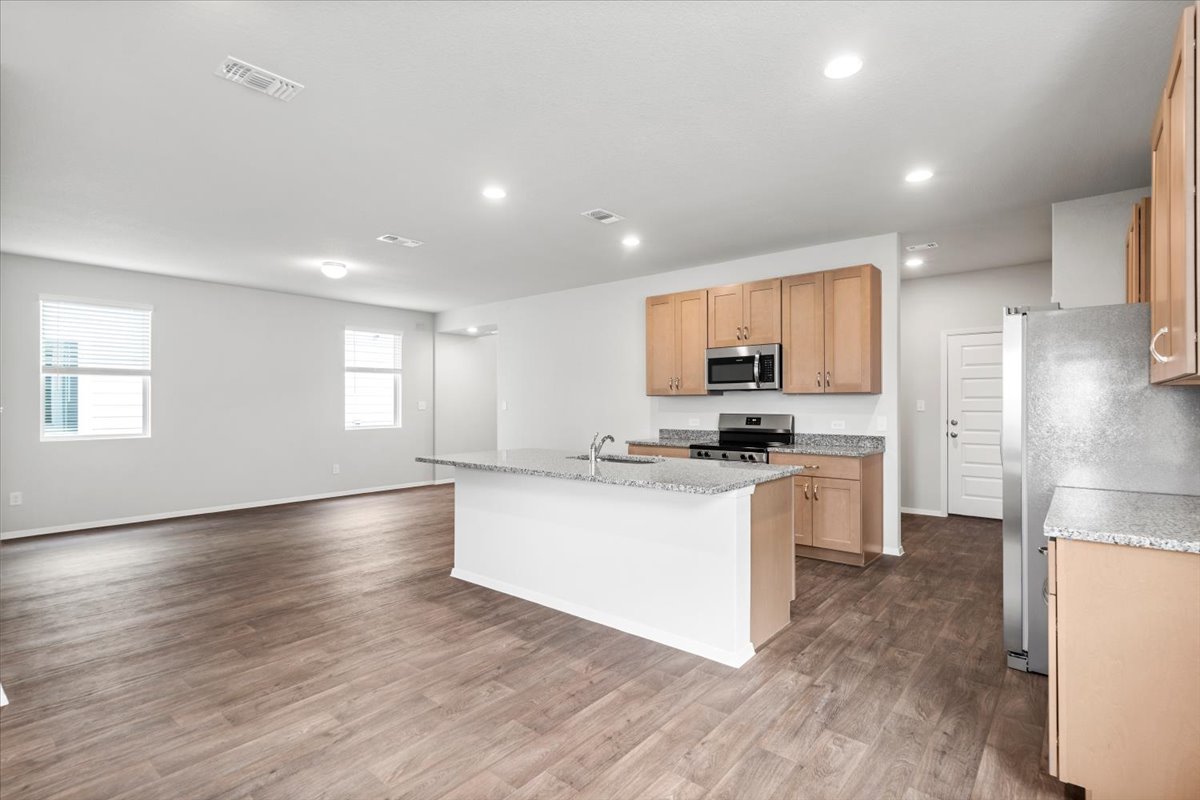 2607 Totley Road Manor, TX 78653 - Photo 4 of 40 Kitchen featuring stainless steel appliances, wood finished floors, a center island with sink, recessed lighting, and light stone countertops
