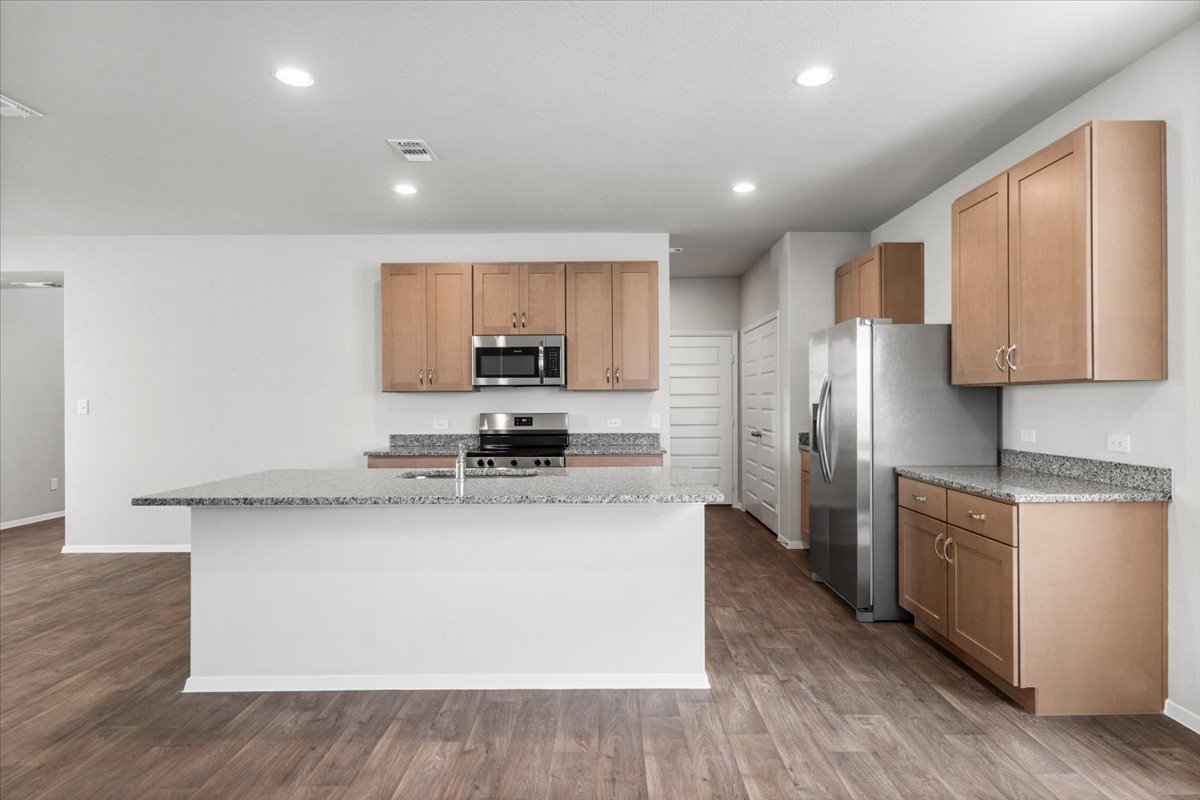 2607 Totley Road Manor, TX 78653 - Photo 5 of 40 Kitchen with a kitchen island with sink, stainless steel appliances, dark wood-style flooring, recessed lighting, and light stone countertops