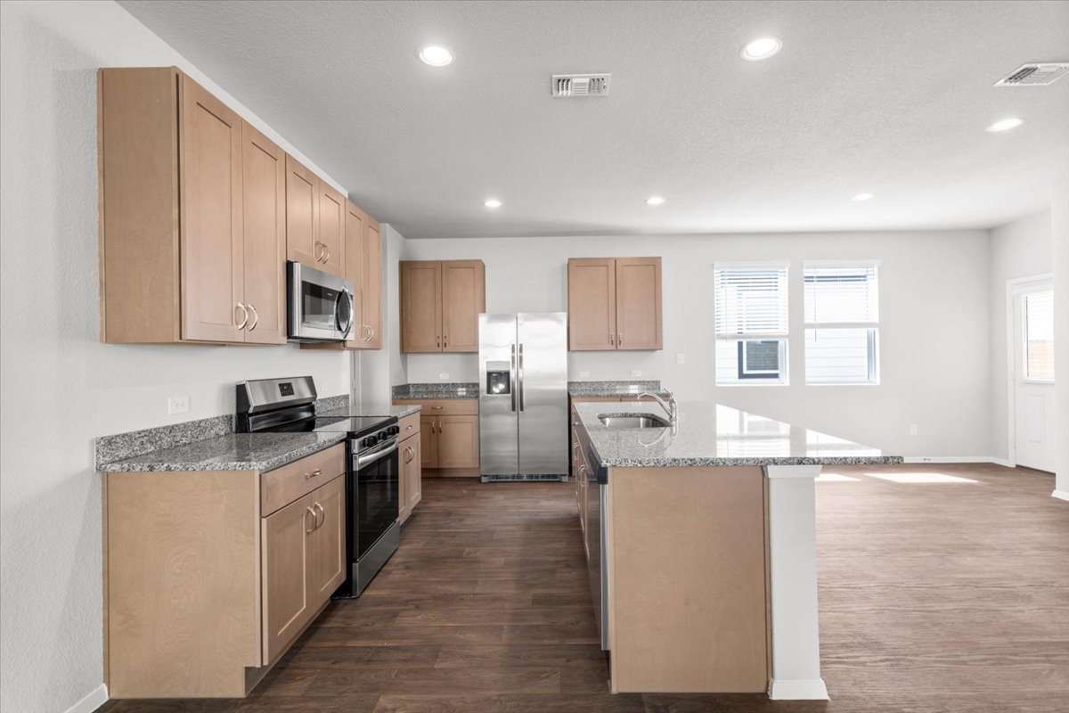 2607 Totley Road Manor, TX 78653 - Photo 7 of 40 Kitchen with appliances with stainless steel finishes, dark wood-type flooring, recessed lighting, light stone countertops, and a kitchen island with sink