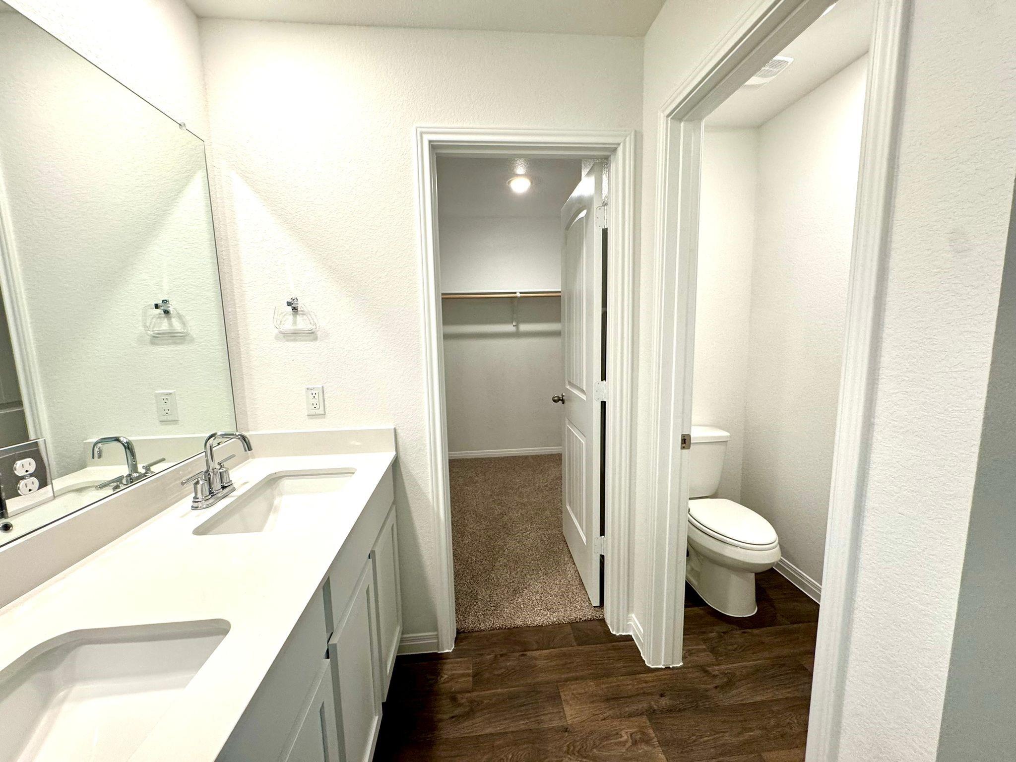 346 Gladiola Loop Kyle, TX 78640 - Photo 13 of 16 Bathroom with double vanity, dark wood-style floors, a spacious closet, and a textured wall