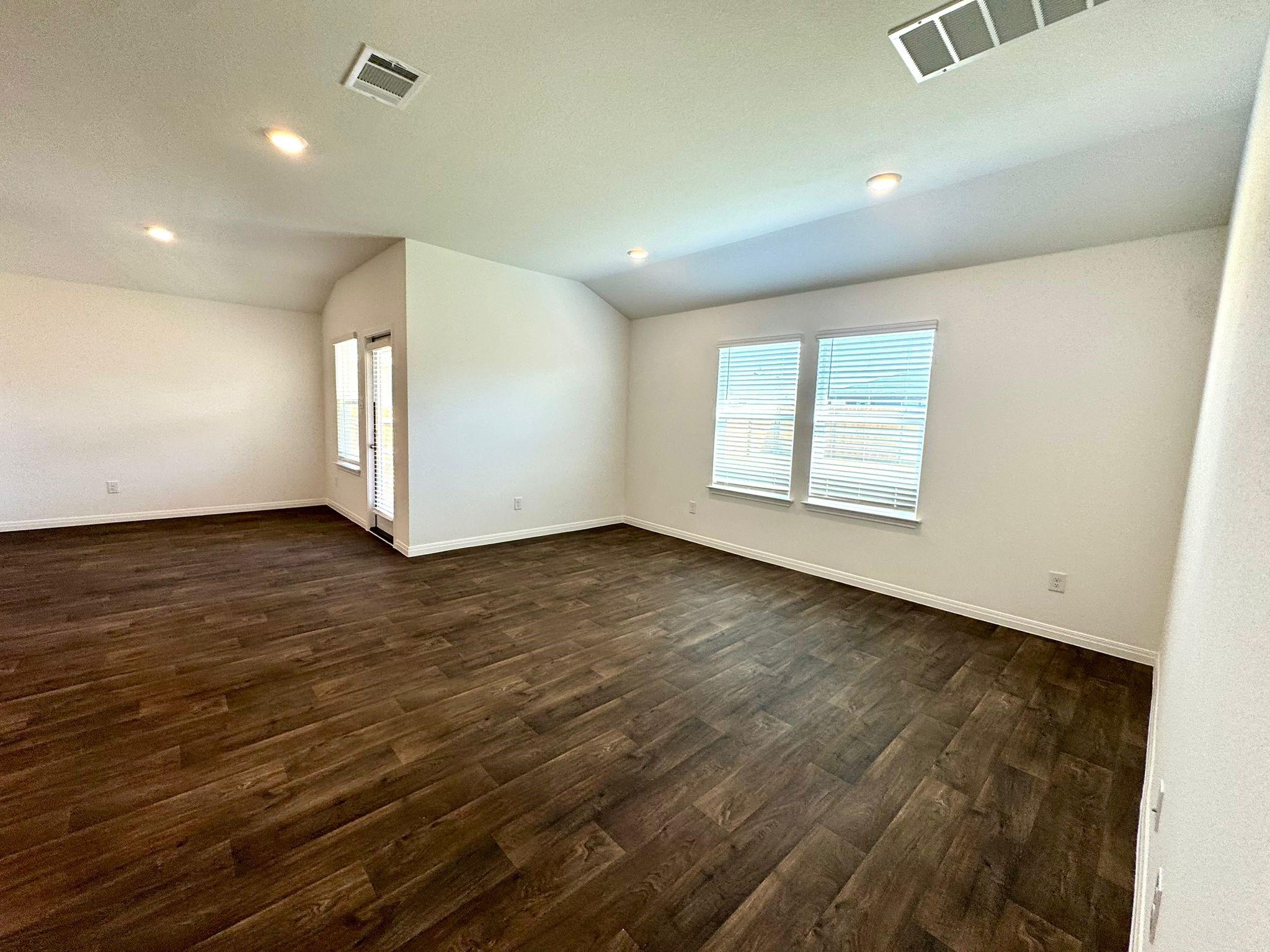 346 Gladiola Loop Kyle, TX 78640 - Photo 5 of 16 Empty room featuring healthy amount of natural light, dark wood-style floors, vaulted ceiling, and recessed lighting