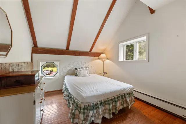 a bedroom with a bed a dresser and potted plants with the wooden floor