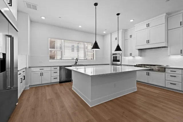 a large kitchen with stainless steel appliances a large counter top a sink a window and cabinets