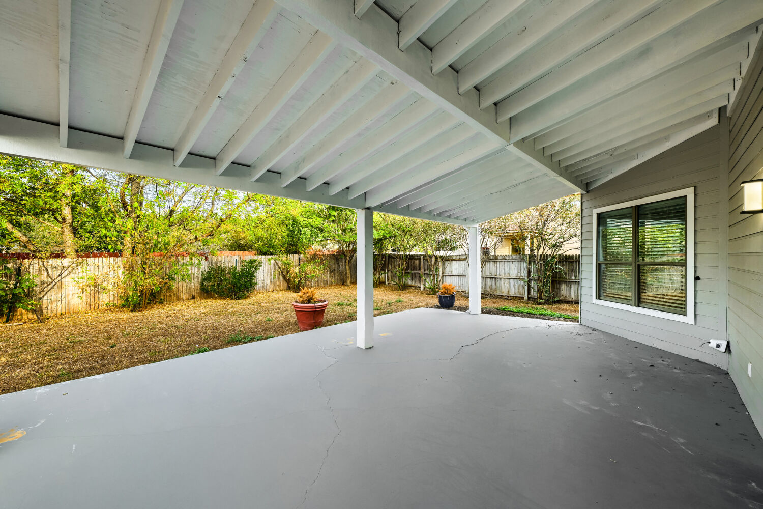 4508 Peach Grove Road Austin, TX 78744 - Photo 3 of 22 An inviting covered patio looks out over a fenced yard bordered by mature trees.