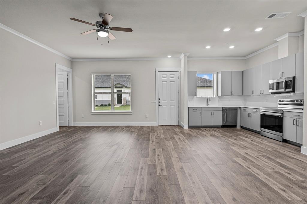 a view of an empty room with kitchen and window