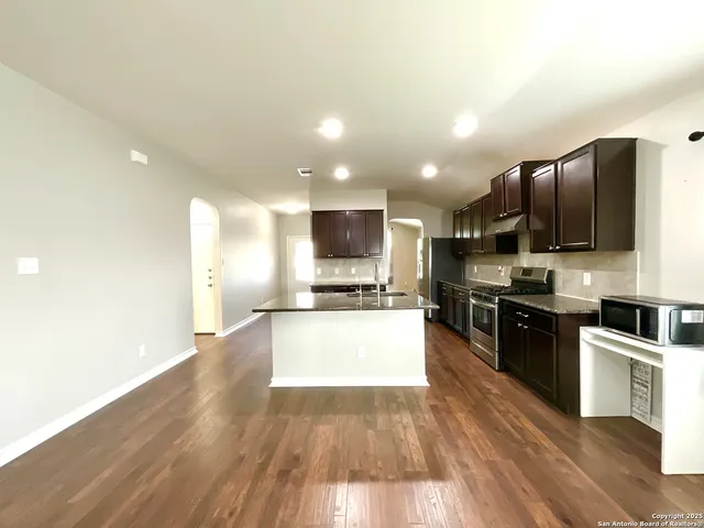 a kitchen with stainless steel appliances granite countertop a stove top oven a sink dishwasher and a refrigerator with wooden floor