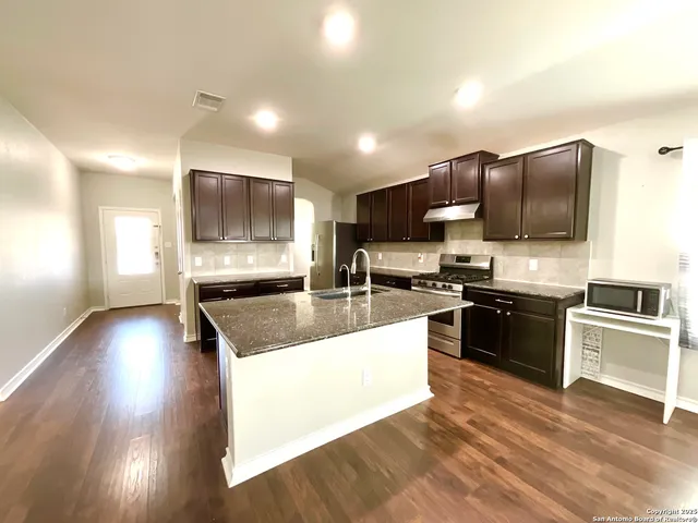 a large kitchen with a large counter top stainless steel appliances and wooden floor