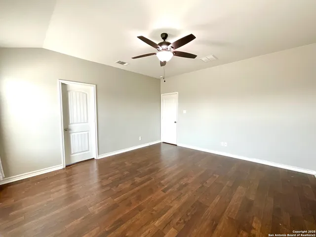 an empty room with wooden floor fan and windows