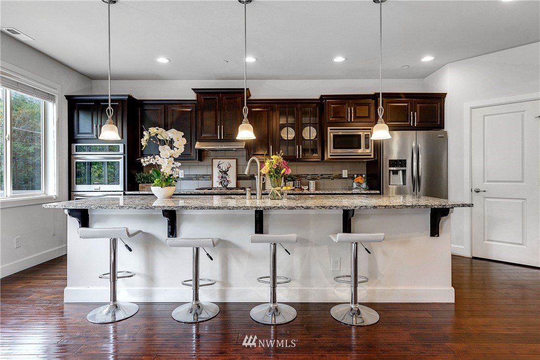 20057 94th Avenue Northeast, Unit 36 Bothell, WA 98011 - Photo 5 of 31 a kitchen with stainless steel appliances kitchen island granite countertop a stove and white cabinets with wooden floor