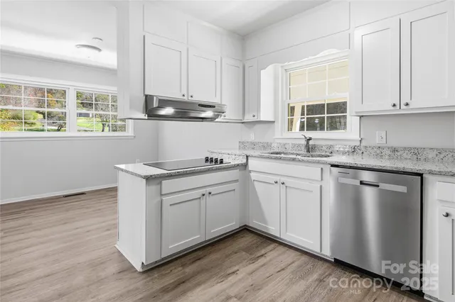 a kitchen with stainless steel appliances granite countertop a stove a sink and white cabinets with wooden floor