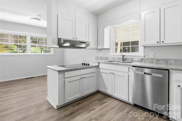 a kitchen with stainless steel appliances granite countertop a stove a sink and white cabinets with wooden floor