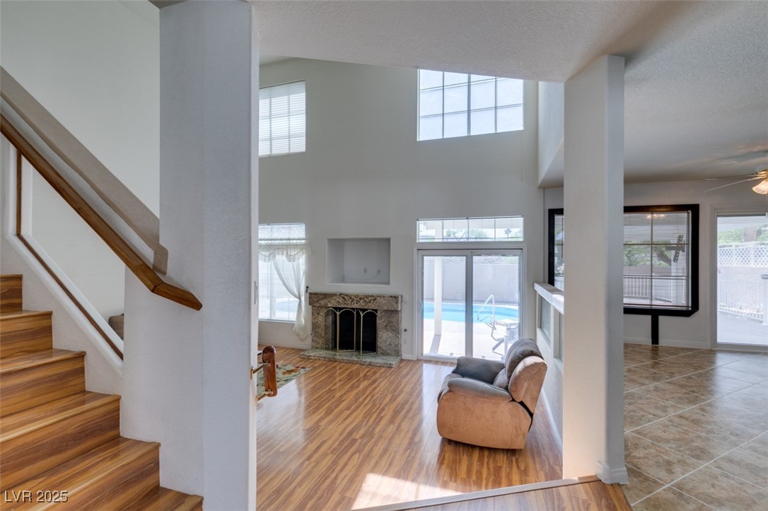 6 High Sierra Henderson, NV 89074 - Photo 17 of 56 Tiled living area featuring stairs, a ceiling fan, a fireplace with raised hearth, and a high ceiling