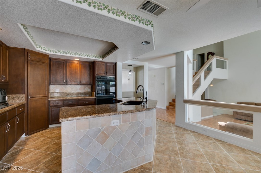 6 High Sierra Henderson, NV 89074 - Photo 32 of 56 Kitchen featuring a sink, light tile patterned floors, a raised ceiling, backsplash, and dark stone countertops