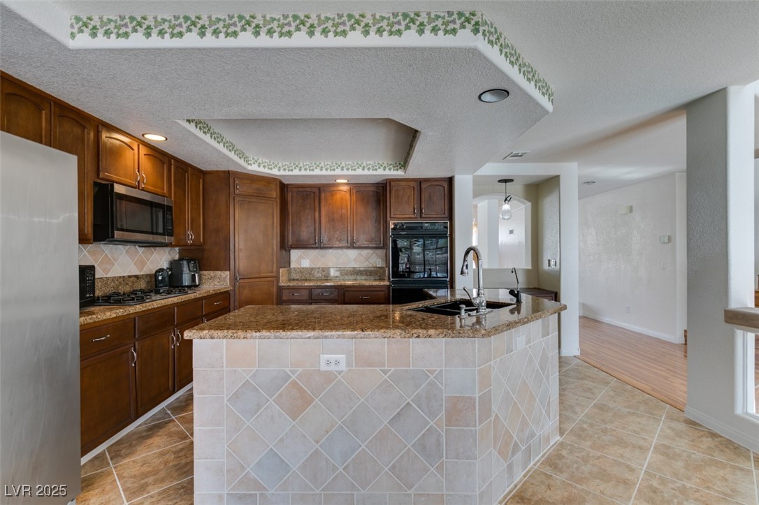 6 High Sierra Henderson, NV 89074 - Photo 33 of 56 Kitchen with appliances with stainless steel finishes, a sink, light tile patterned floors, decorative backsplash, and a textured ceiling