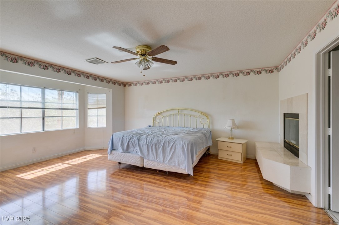 6 High Sierra Henderson, NV 89074 - Photo 42 of 56 Bedroom with light wood-style floors, baseboards, a glass covered fireplace, ceiling fan, and a textured ceiling