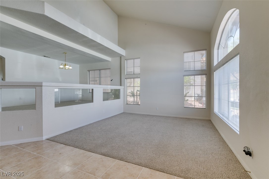 6 High Sierra Henderson, NV 89074 - Photo 5 of 56 Unfurnished living room featuring high vaulted ceiling, carpet floors, a chandelier, tile patterned floors, and baseboards