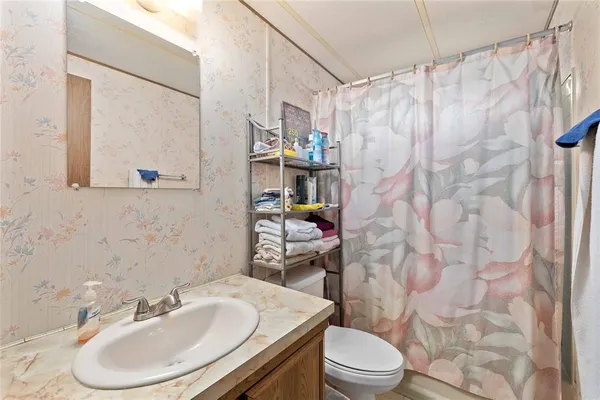 a bathroom with a granite countertop sink a toilet a large mirror a vanity and shower