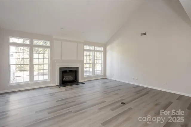an empty room with wooden floor fireplace and windows