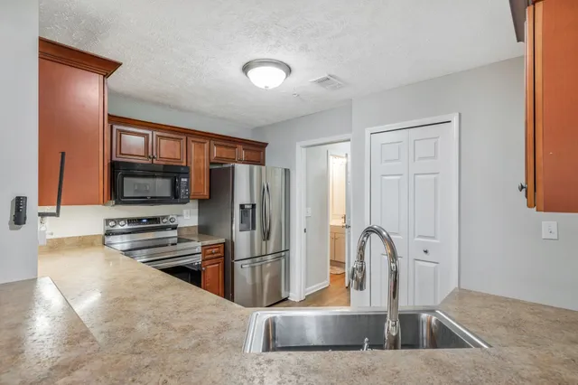 a kitchen with stainless steel appliances granite countertop a refrigerator a stove and a sink with wooden cabinets