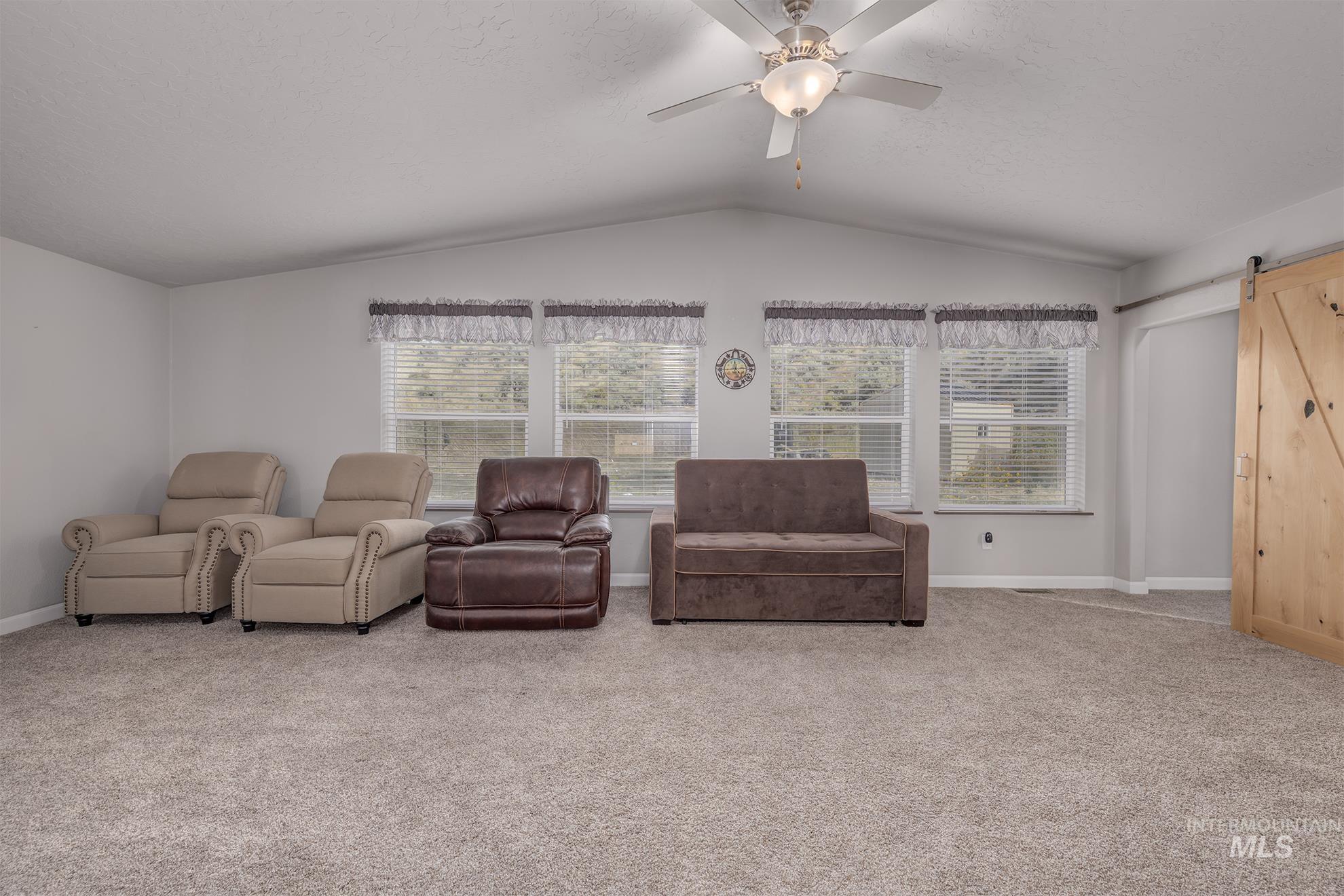 1587 Gentry Lane Weiser, ID 83672 - Photo 17 of 41 Living room featuring a barn door, carpet floors, lofted ceiling, and a ceiling fan