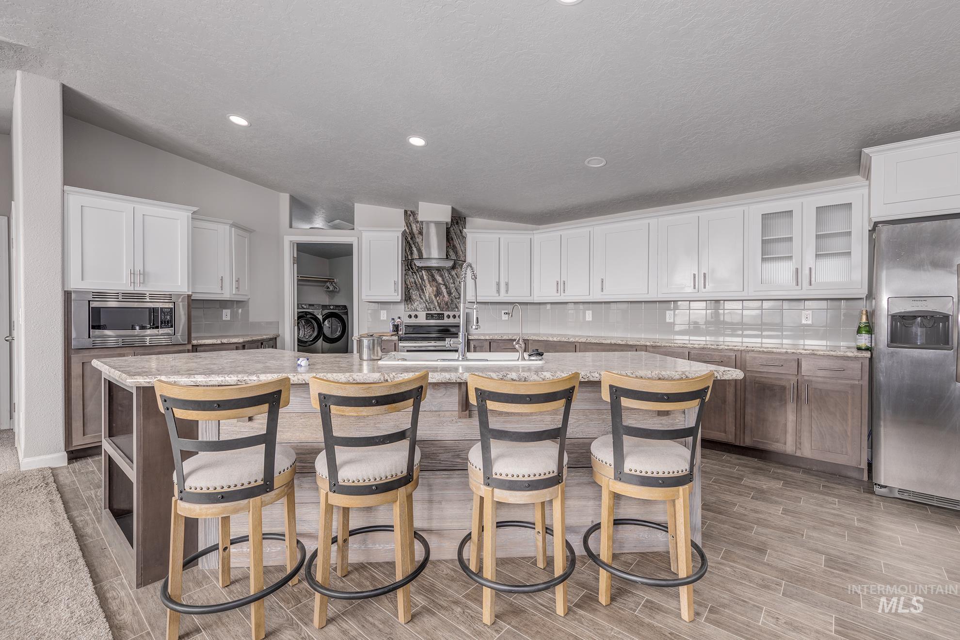 1587 Gentry Lane Weiser, ID 83672 - Photo 9 of 41 Kitchen with decorative backsplash, white cabinets, a center island with sink, stainless steel appliances, and a textured ceiling