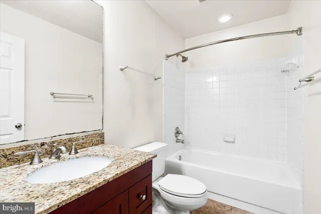 a bathroom with a granite countertop bathtub shower sink vanity mirror and toilet