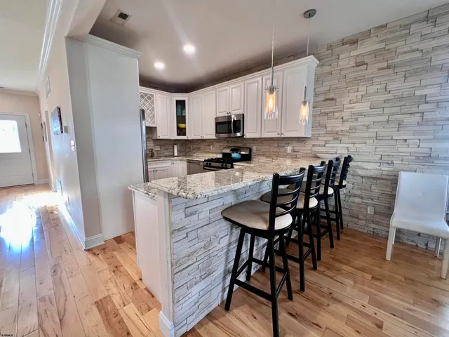 a room with stainless steel appliances kitchen island granite countertop a dining table chairs and a refrigerator