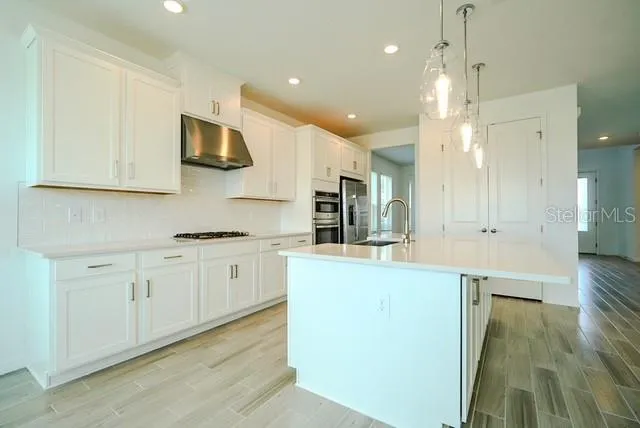 a large kitchen with stainless steel appliances granite countertop a stove a sink a refrigerator and white cabinets with wooden floor