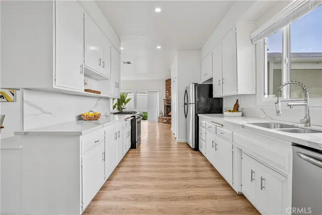 a large kitchen with stainless steel appliances sink a white cabinets and wooden floor