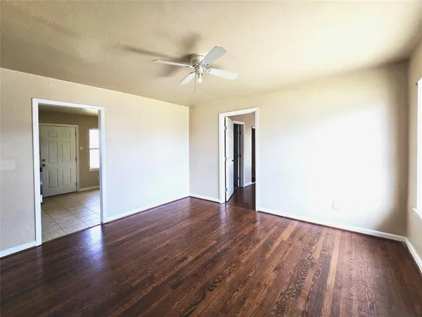 an empty room with wooden floor a ceiling fan and kitchen view