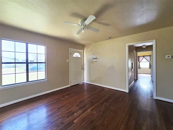 an empty room with wooden floor fan and windows