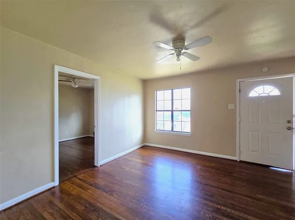 an empty room with wooden floor chandelier fan and windows