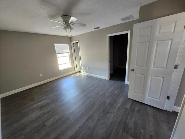 an empty room with wooden floor chandelier fan and windows