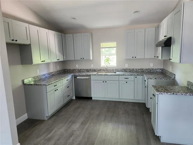 a kitchen with granite countertop white cabinets sink and dishwasher with wooden floor