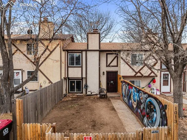 a view of a white house with a large tree and wooden fence