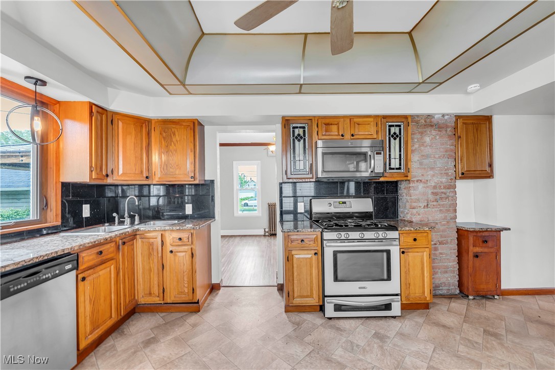 3374 Fulton Road Cleveland, OH 44109 - Photo 11 of 27 Kitchen featuring stainless steel appliances, brown cabinetry, decorative light fixtures, light stone countertops, and tasteful backsplash